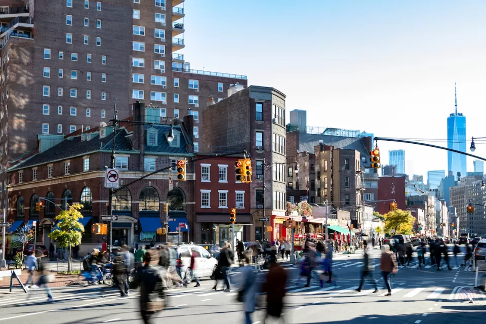 Street scene in Greenwich Village, New York City with people walking through busy intersection and new WTC tower in background.